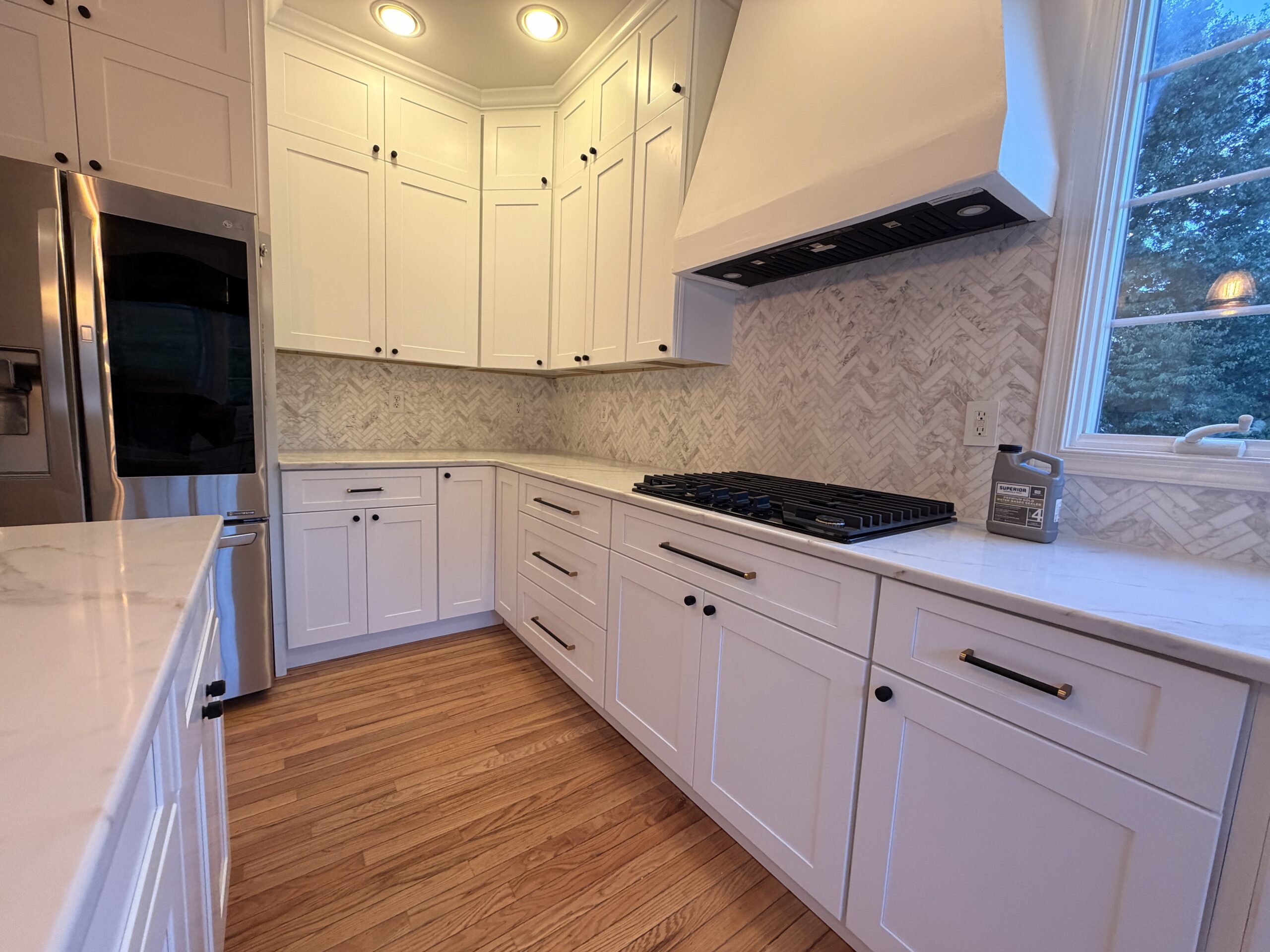 Herringbone backsplash, white cabinets and dark hardware beside the cooktop